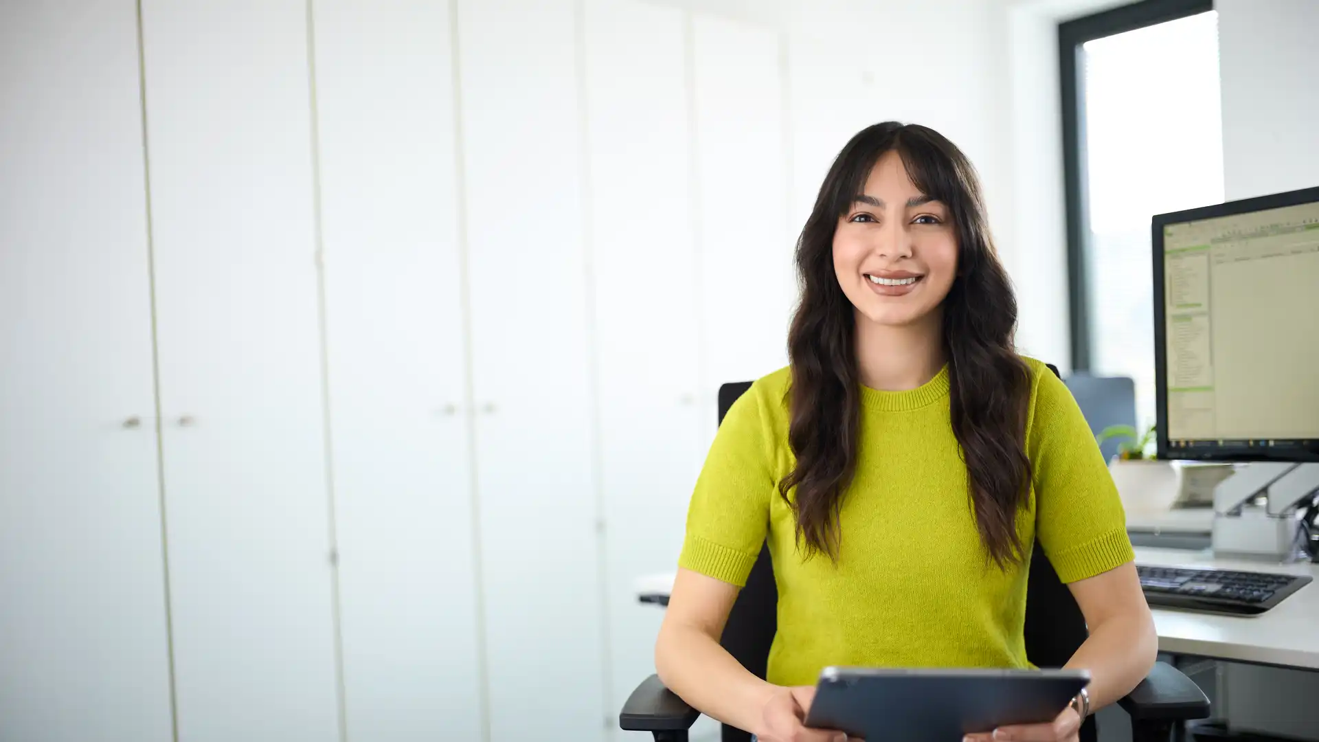 Eine Frau sitzt an einem Schreibtisch und hält ein Tablet in den Händen