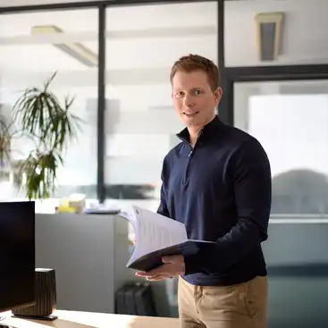 Ein Mann steht in einem Büro und hält Unterlagen in den Händen