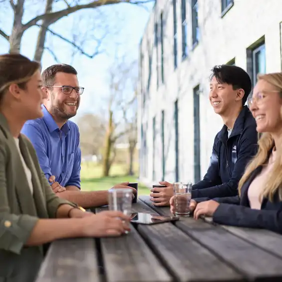 Eine Gruppe von Menschen sitzt im Freien an einem Holztisch