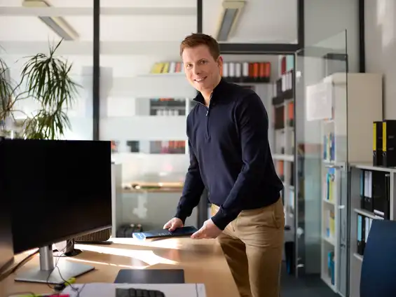 Ein Mann steht an einem Schreibtisch und hält Unterlagen in der Hand